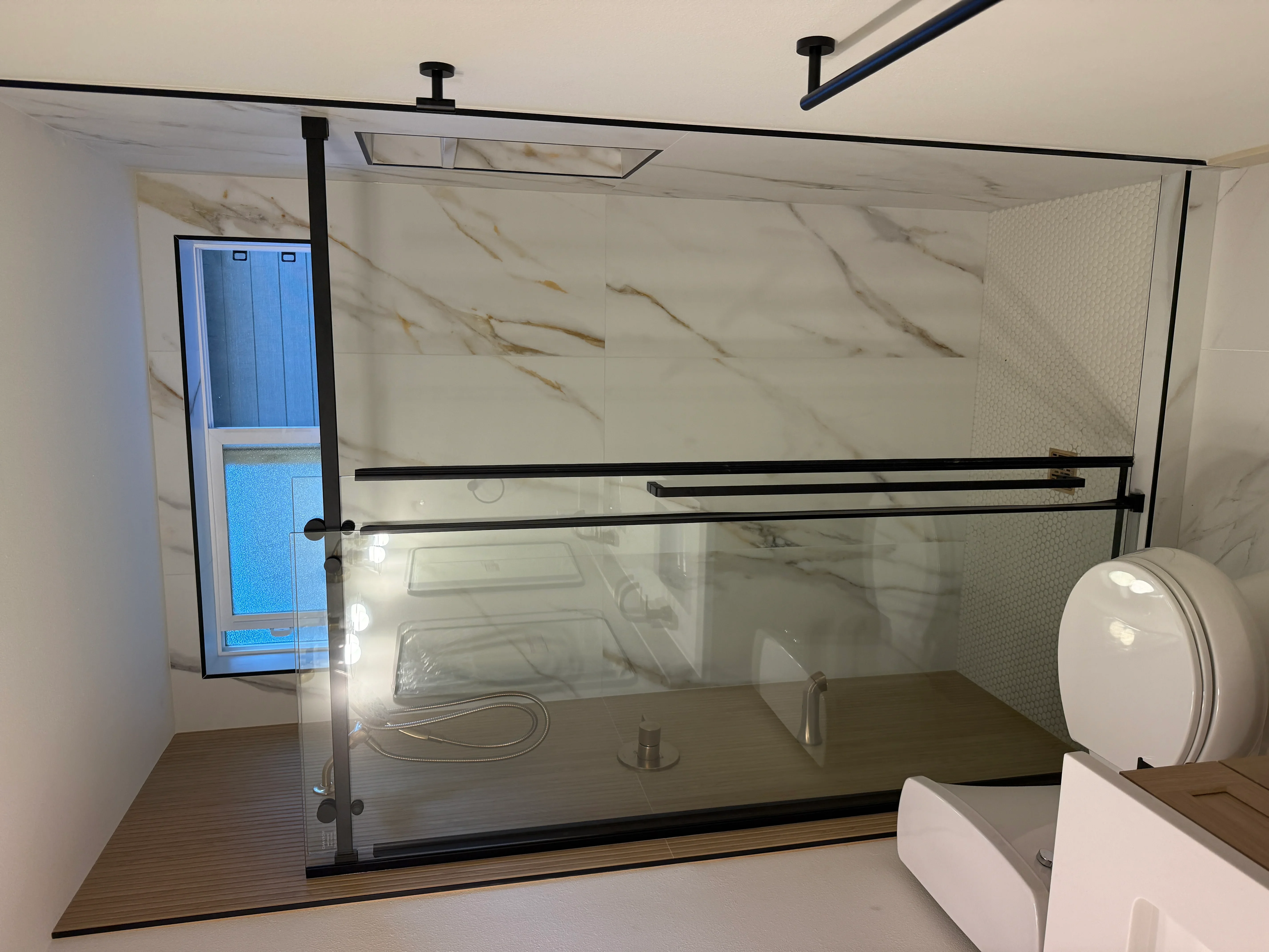 Frameless glass shower enclosure with marble tile walls and black metal hardware