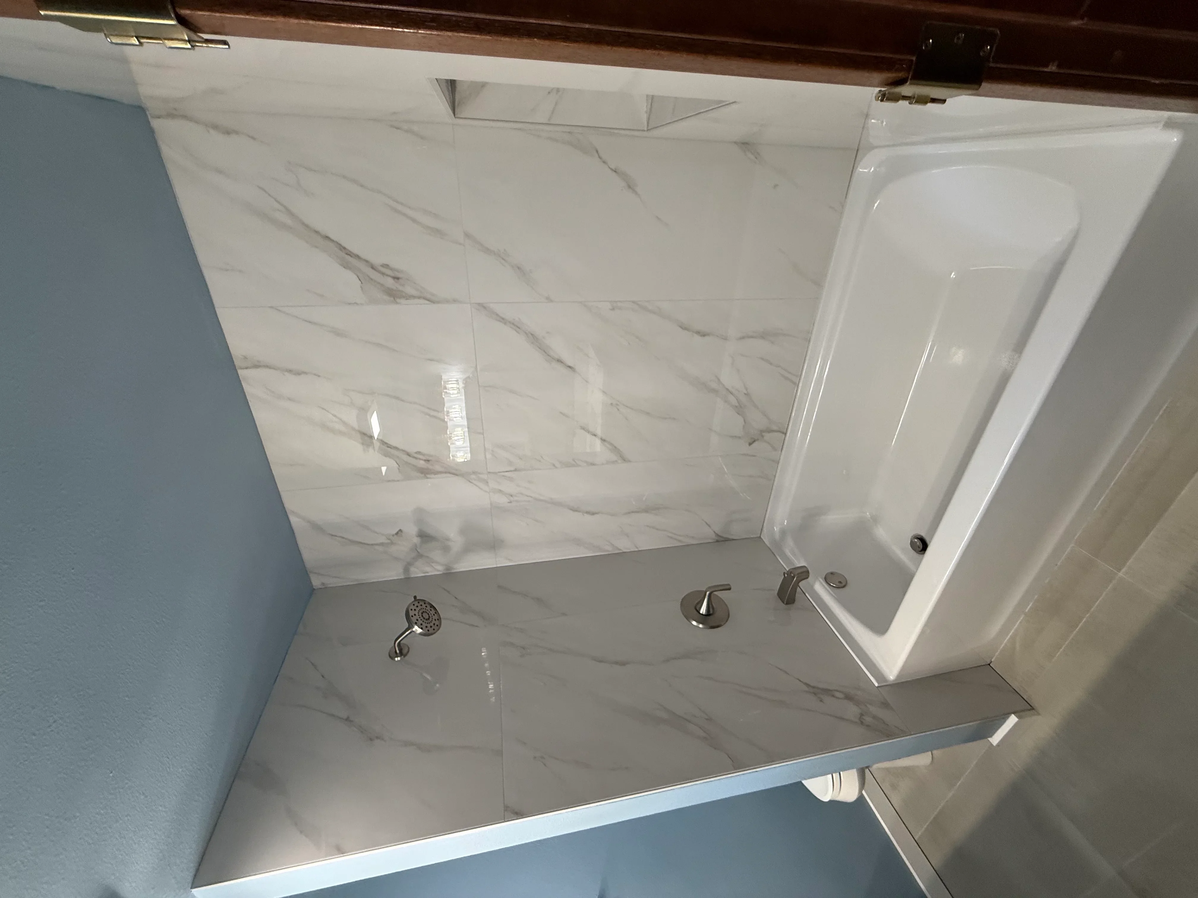 Marble-look porcelain tile shower with frameless glass door and brushed nickel fixtures